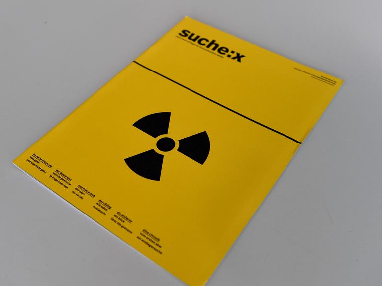 Eine Broschüre mit der Aufschrift "Suche:X" und einem Strahlenwarnzeichen liegt bei einer Pressekonferenz auf einem Tisch. 