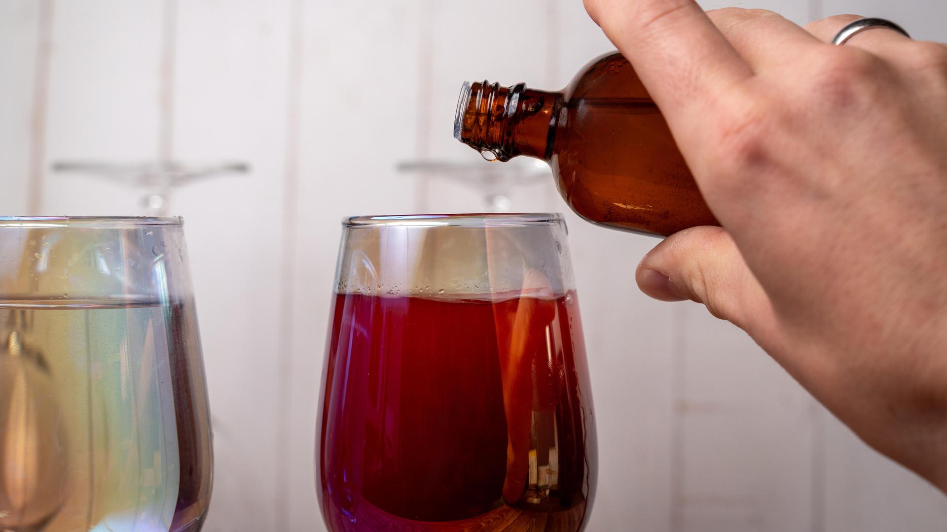 Eine Hand gießt eine Flüssigkeit aus einer braunen Flasche in ein Wein-Glas.
