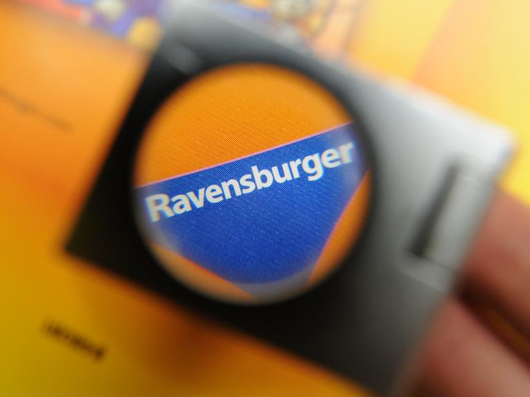 Das blaue Dreiecks-Logo von Ravensburger durch eine Lupe fotografiert