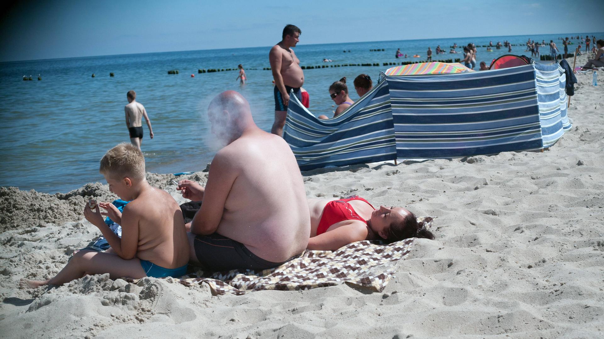 Eine Familie am Strand. Der Mann raucht, sein Sohn sitzt daneben. Eine Familie am Strand. Der Mann raucht, sein Sohn sitzt daneben.