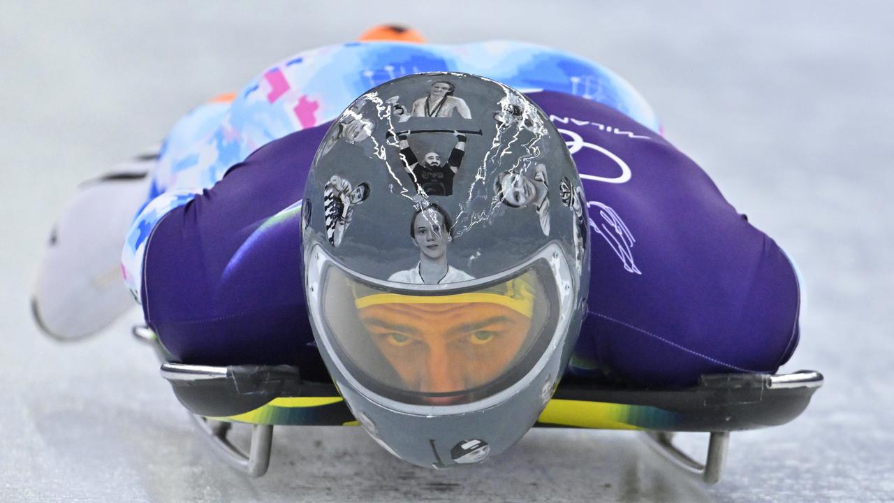 Der ukrainische Skeleton-Fahrer Wladyslaw Heraskewytsch bei einer Testfahrt auf dem Eis. Er trägt einen grauen Helm mit Bildern von 24 gefallene ukrainische Sportlern.