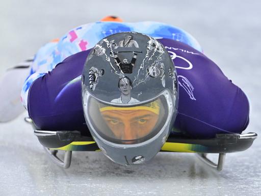 Der ukrainische Skeleton-Fahrer Wladyslaw Heraskewytsch bei einer Testfahrt auf dem Eis. Er trägt einen grauen Helm mit Bildern von 24 gefallene ukrainische Sportlern.