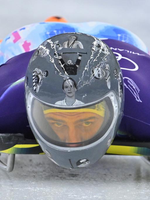 Der ukrainische Skeleton-Fahrer Wladyslaw Heraskewytsch bei einer Testfahrt auf dem Eis. Er trägt einen grauen Helm mit Bildern von 24 gefallene ukrainische Sportlern.