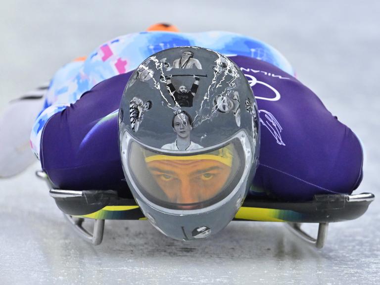 Der ukrainische Skeleton-Fahrer Wladyslaw Heraskewytsch bei einer Testfahrt auf dem Eis. Er trägt einen grauen Helm mit Bildern von 24 gefallene ukrainische Sportlern.