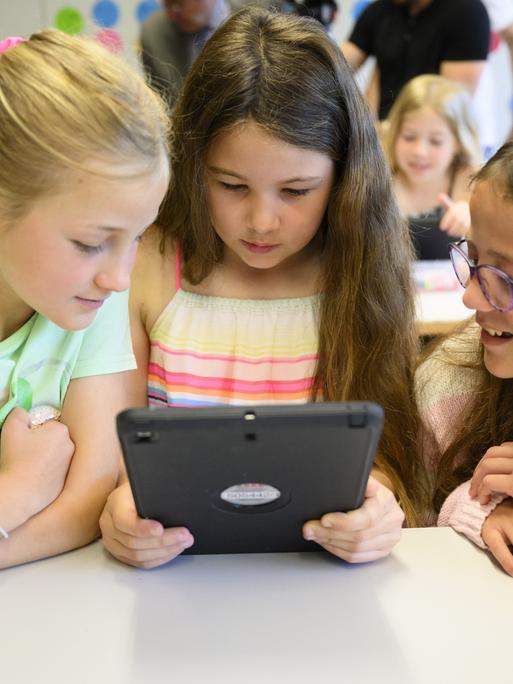 Drei Mädchen sitzen im Klassenraum und starren auf ein Tablet