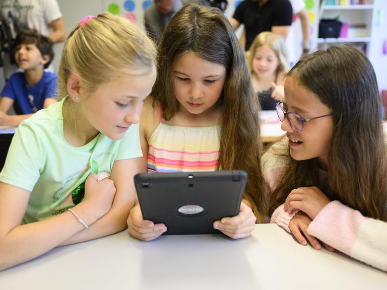 Drei Mädchen sitzen im Klassenraum und starren auf ein Tablet