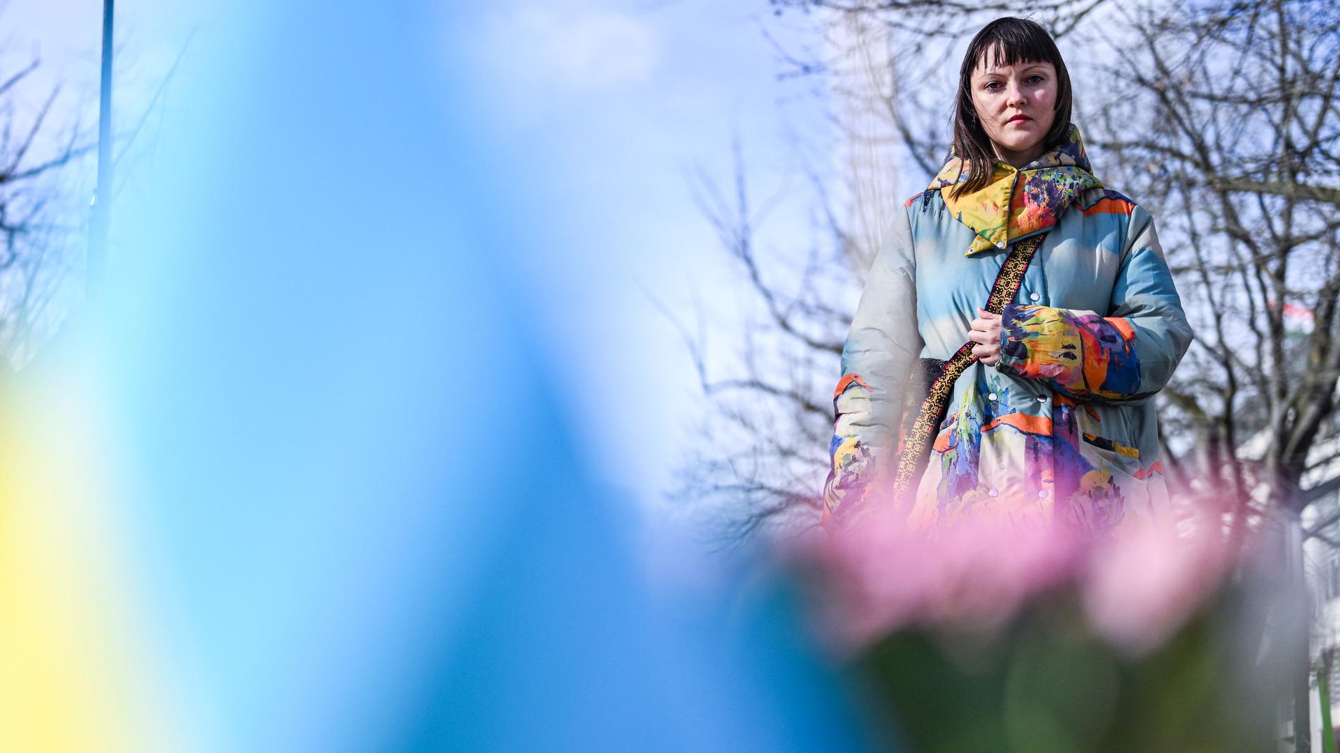 Eine Frau schaut auf Blumen und eine ukrainische Flagge, die im Vordergrund in der Unschärfe zu sehen sind.