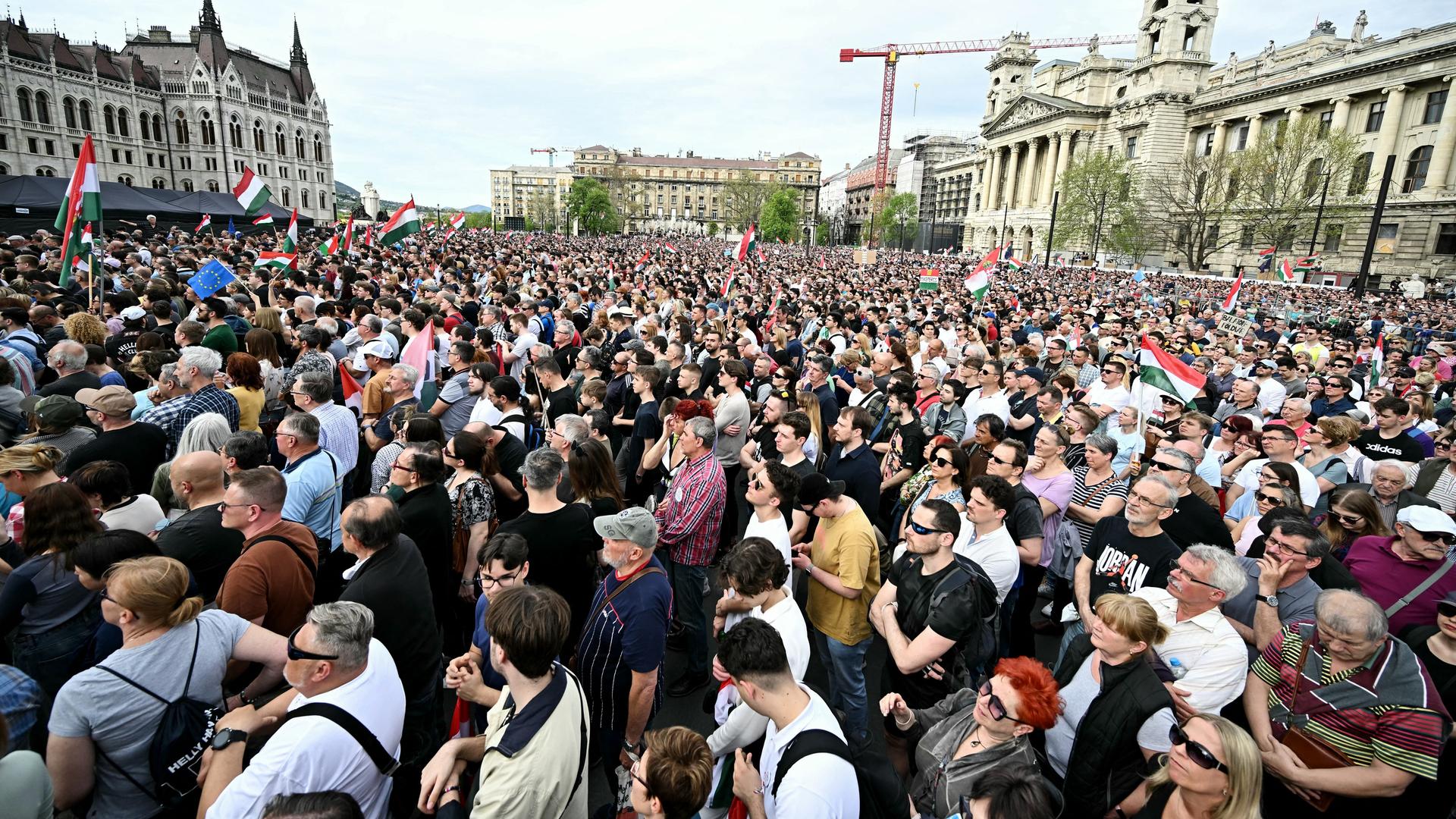 Auf einem großen Platz in Budapest haben sich viele Menschen versammelt. Auch einige ungarische Flaggen sind zu sehen.