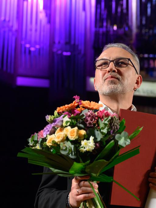 Der belarussische Schriftsteller Alhierd Bacharevic steht mit einem Blumenstrauß auf der Bühne.