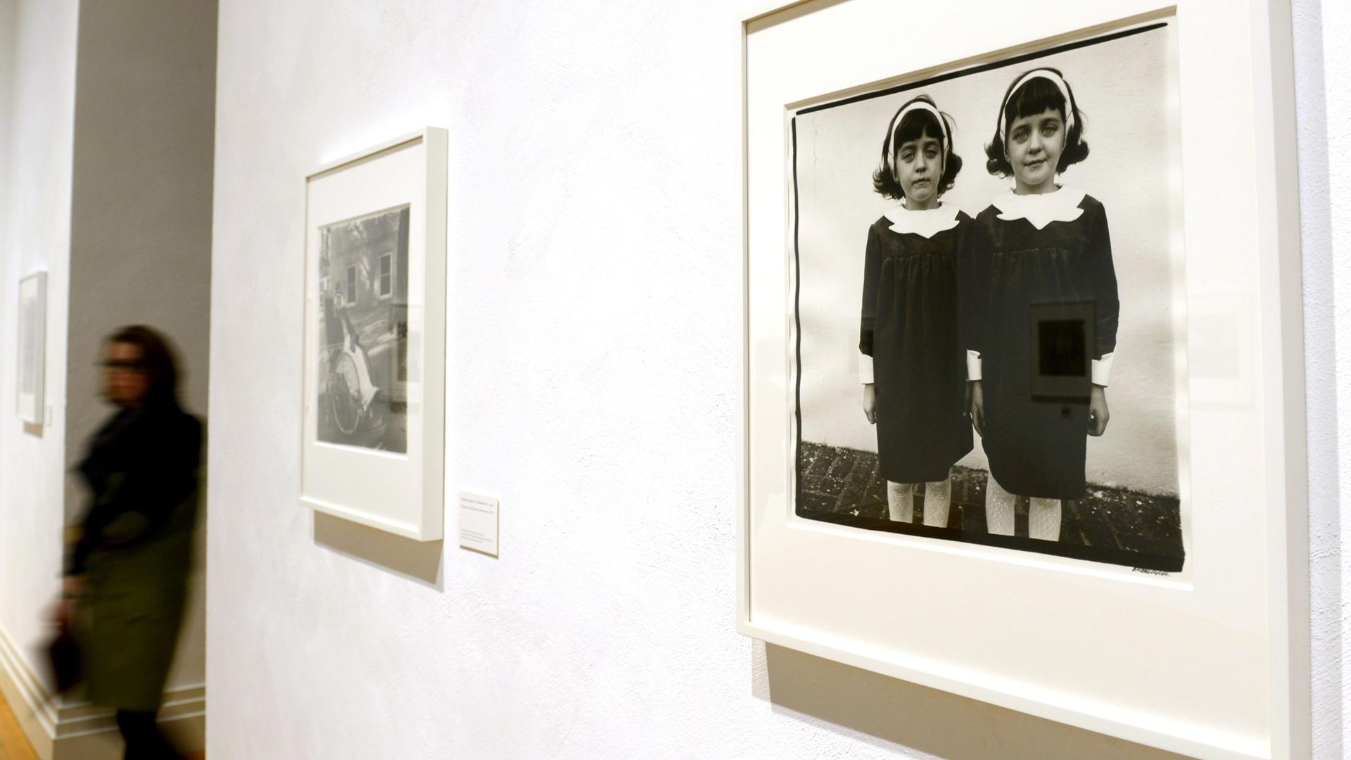 Eine Schwarzweiß-Fotografie zeigt eineiige Zwillinge. Die Mädchen tragen schwarze Kleider und weiße Haarbänder. Das Bild wurde 2012  in einer "Diane Arbus"-Ausstellung im Martin-Gropius-Bau in Berlin gezeigt.