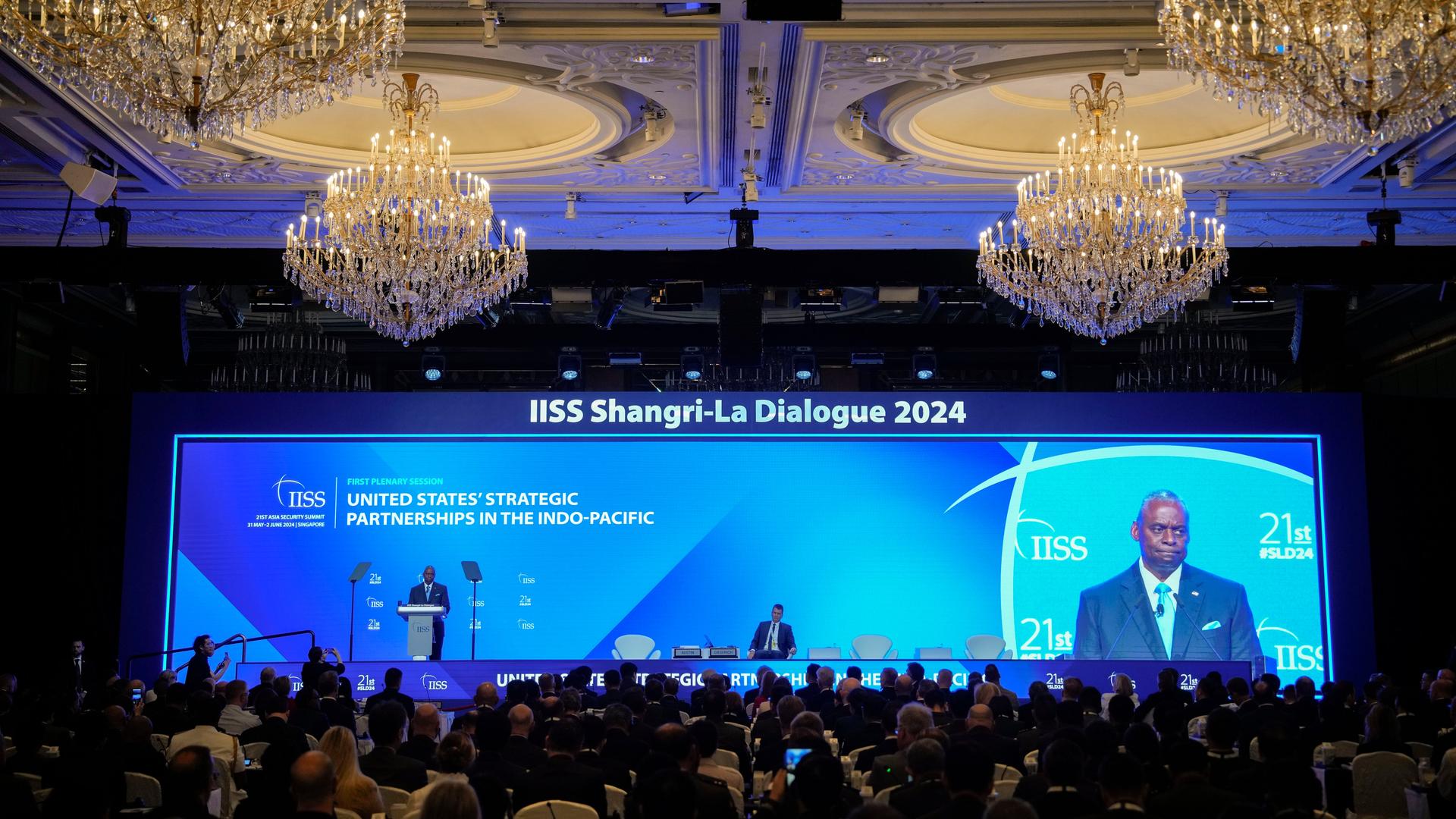 US-Verteidigungsminister Austin spricht bei der Sicherheitstagung in Singapur. Er steht auf einer Bühne, hinter ihm eine große Leinwand, auf der er zu sehen ist; im Vordergrund stehen die Teilnehmer der Konferenz. US-Verteidigungsminister Austin spricht bei der Sicherheitstagung in Singapur. Er steht auf einer Bühne, hinter ihm eine große Leinwand, auf der er zu sehen ist; im Vordergrund stehen die Teilnehmer der Konferenz.