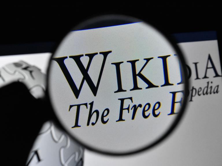 Illustration: Das Logo von Wikipedia durch eine Lupe gesehen, mit dem Wort "Free" auf dem Bildschirm.