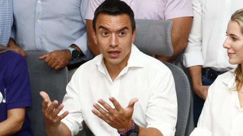 Der ecuadorianische Präsidentschaftskandidat Daniel Noboa sitzt – im weißen Hemd – auf einem Stuhl vor einem Tisch und gestikuliert beim Sprechen mit den Händen. Um ihn herum Frauen und Männer. 