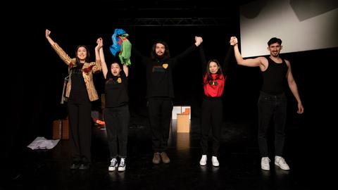 Fünf junge Mitglieder der Theatergruppe stehen mit erhobenen Armen jubelnd auf der Bühne.