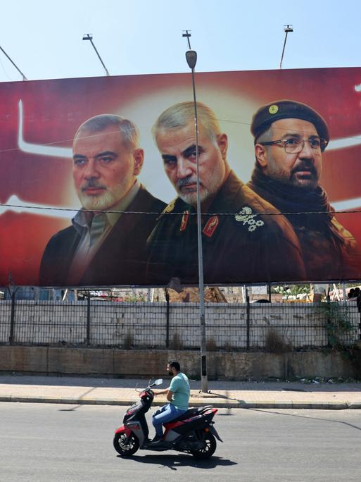 An einer Straße steht ein Banner mit Porträts der getöteten Milizenführer Ismail Haniyeh, Qasem Soleimani und Fuad Shukr.