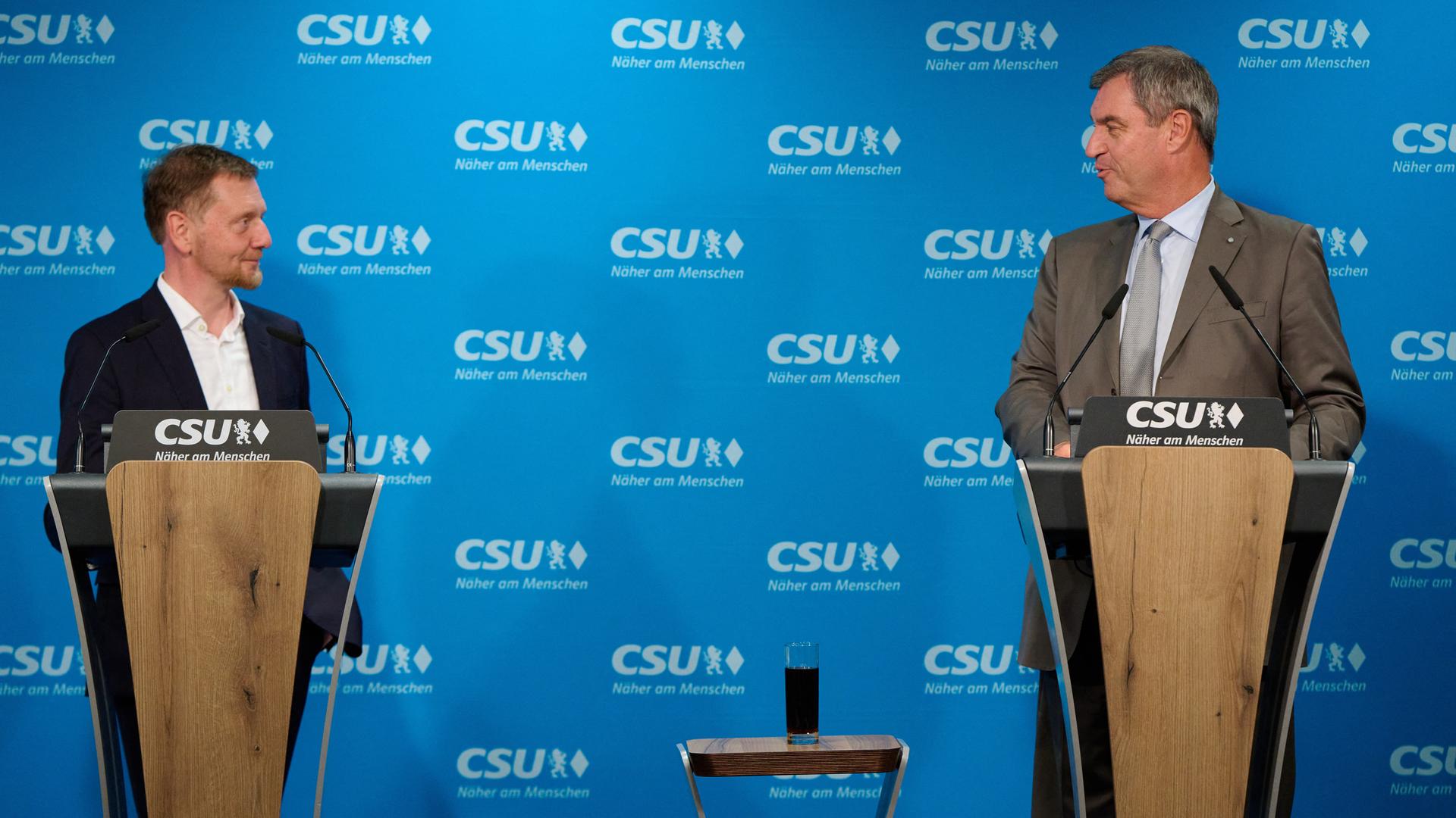 Markus Söder und Michael Kretschmer stehen an zwei nebeneinander stehenden Stehpulten und sehen sich an. An der Wand hinter ihnen prangt das Logo der CSU. Markus Söder und Michael Kretschmer stehen an zwei nebeneinander stehenden Stehpulten und sehen sich an. An der Wand hinter ihnen prangt das Logo der CSU.