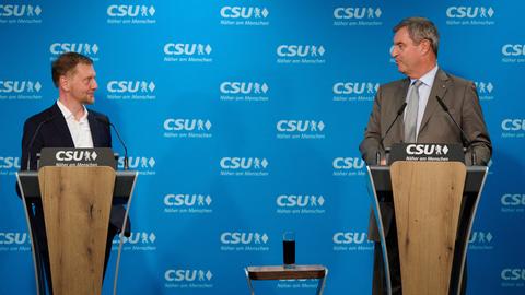 Markus Söder und Michael Kretschmer stehen an zwei nebeneinander stehenden Stehpulten und sehen sich an. An der Wand hinter ihnen prangt das Logo der CSU.