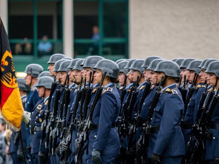 Appell zur Verabschiedung des 124. Offizierslehrgangs der Luftwaffe der Bundeswehr in der Kaserne in Fürstenfeldbruck. Soldaten in blauen Uniformen und Helmen stehen in Formation mit Gewehren. Neben ihnen eine Fahne mit dem Symbol des Bundesadlers.