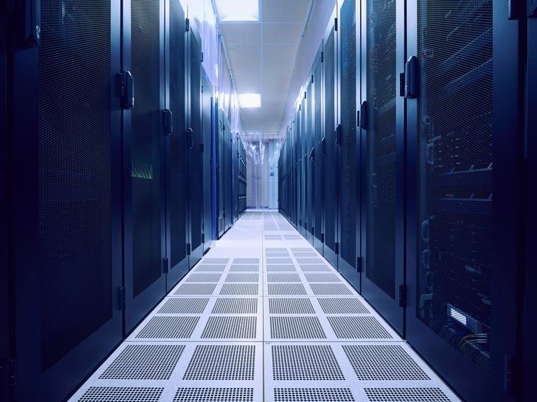 Blick in einen leeren Serverraum. Links und rechts stehen dunkle Serverschränke.