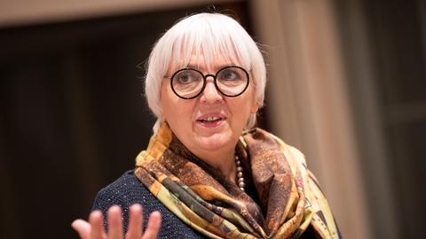 Kulturstaatsministerin Claudia Roth mit schwarzer Brille und buntem Tuch gestikuliert in die Kamera.