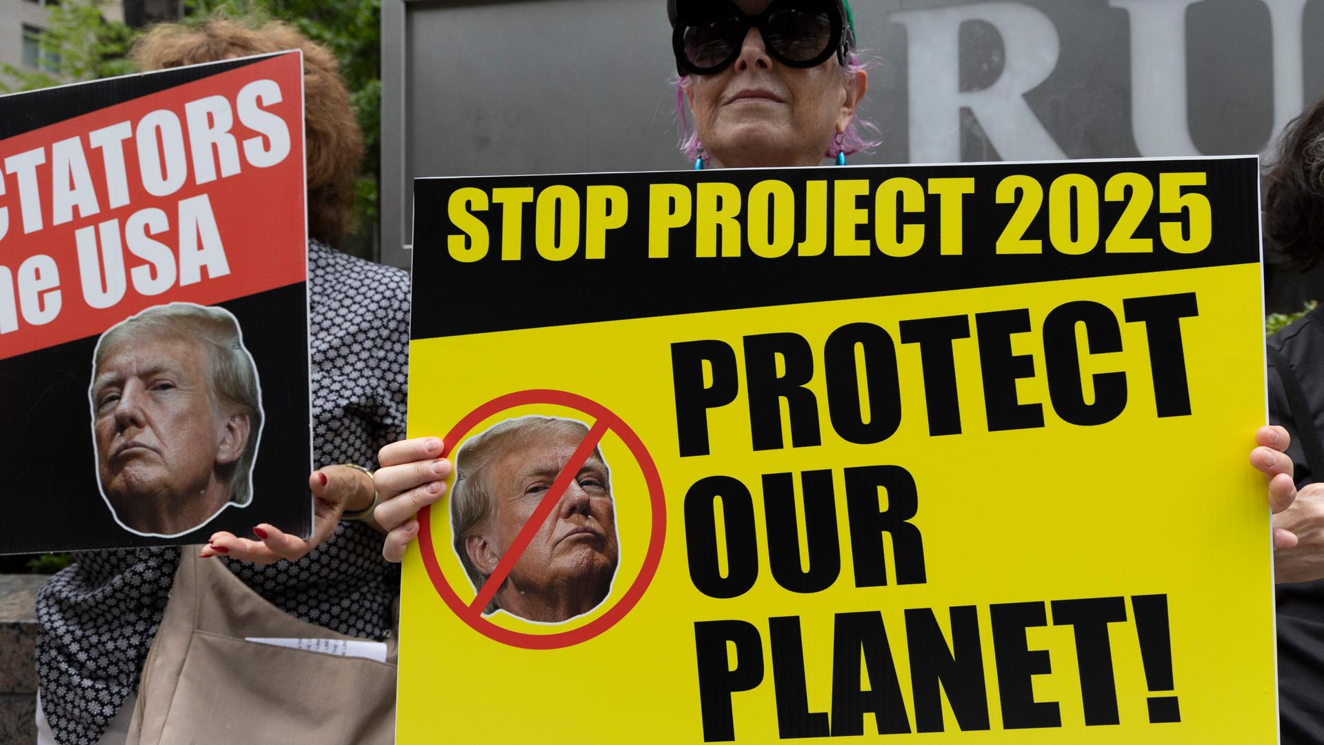 Ein Anti-Trump-Protestler der Aktivistengruppe Rise & Resist hält vor dem Trump International Hotel & Tower ein Schild mit einem durchgestrichenen Bild von Trump mit der Aufschrift "STOP PROJECT 2025 PROTECT OUR PLANET! 