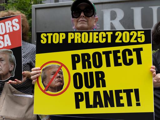 Ein Anti-Trump-Protestler der Aktivistengruppe Rise & Resist hält vor dem Trump International Hotel & Tower ein Schild mit einem durchgestrichenen Bild von Trump mit der Aufschrift "STOP PROJECT 2025 PROTECT OUR PLANET! 