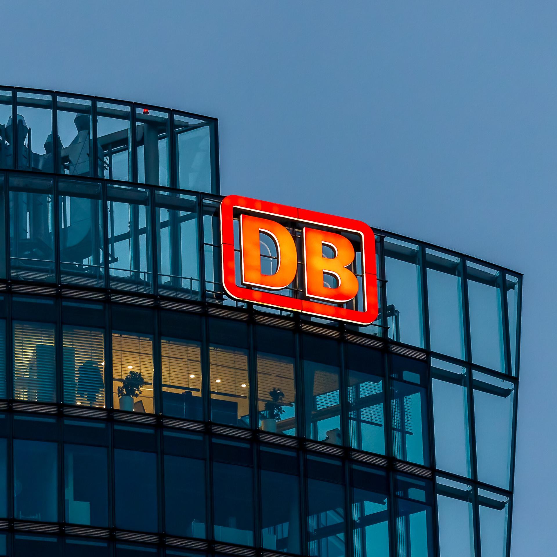 Das Bild zeigt die Vorstandsetage der Zentrale der Deutschen Bahn in der Daemmerung, außen am Gebäude prangt das rote DB-Logo.