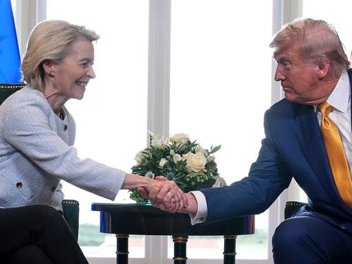 Donald Trump and Ursula von der Leyen schütteln sich sitzend die Hände.
