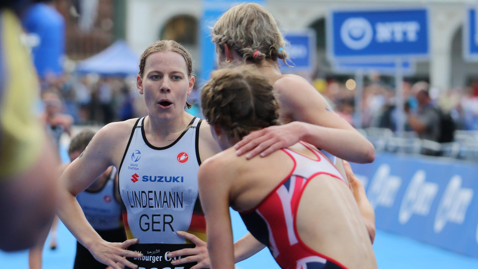 Laura Lindemann steht neben zwei anderen Triathletinnen in Hamburg am Ziel. Sie pustet in die Luft und stützt die Arme in der Taille ab.