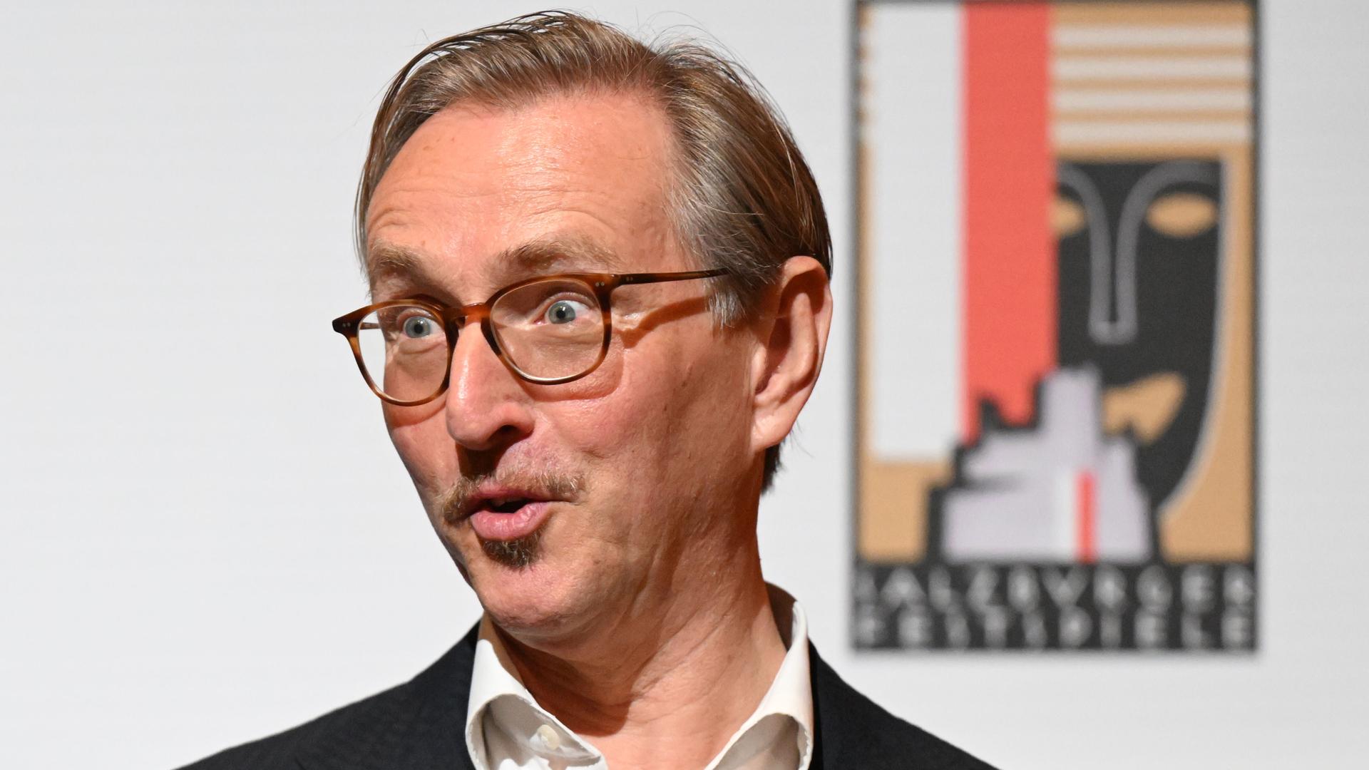 Der designierte Intendant der Salzburger Festspiele Peter de Caluwe schaut lächelnd mit spitzem Mund zur Seite.