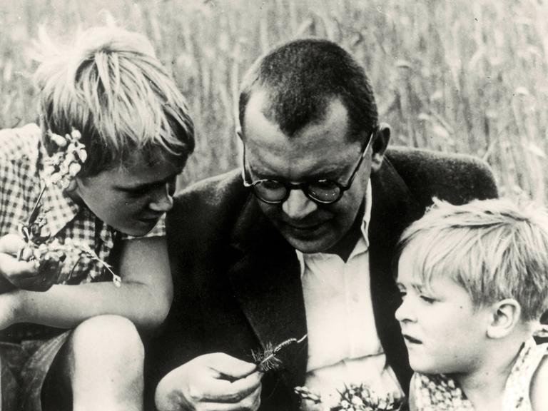 Hans Fallada sitzt mit seinen Kindern  Ulli und Lore in Carwitz im heutigen Mecklenburg-Vorpommern auf einer Wiese und schaut sich eine Raupe mit ihnen an.