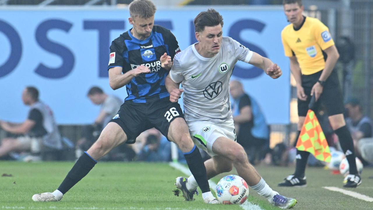 Das Bild zeigt einen Zweikampf zwischen Fußball-Profis direkt an der Seitenauslinie. Im Hintergrund ist ein Schiedsrichter-Assistent mit einer Signal-Fahne zu sehen
