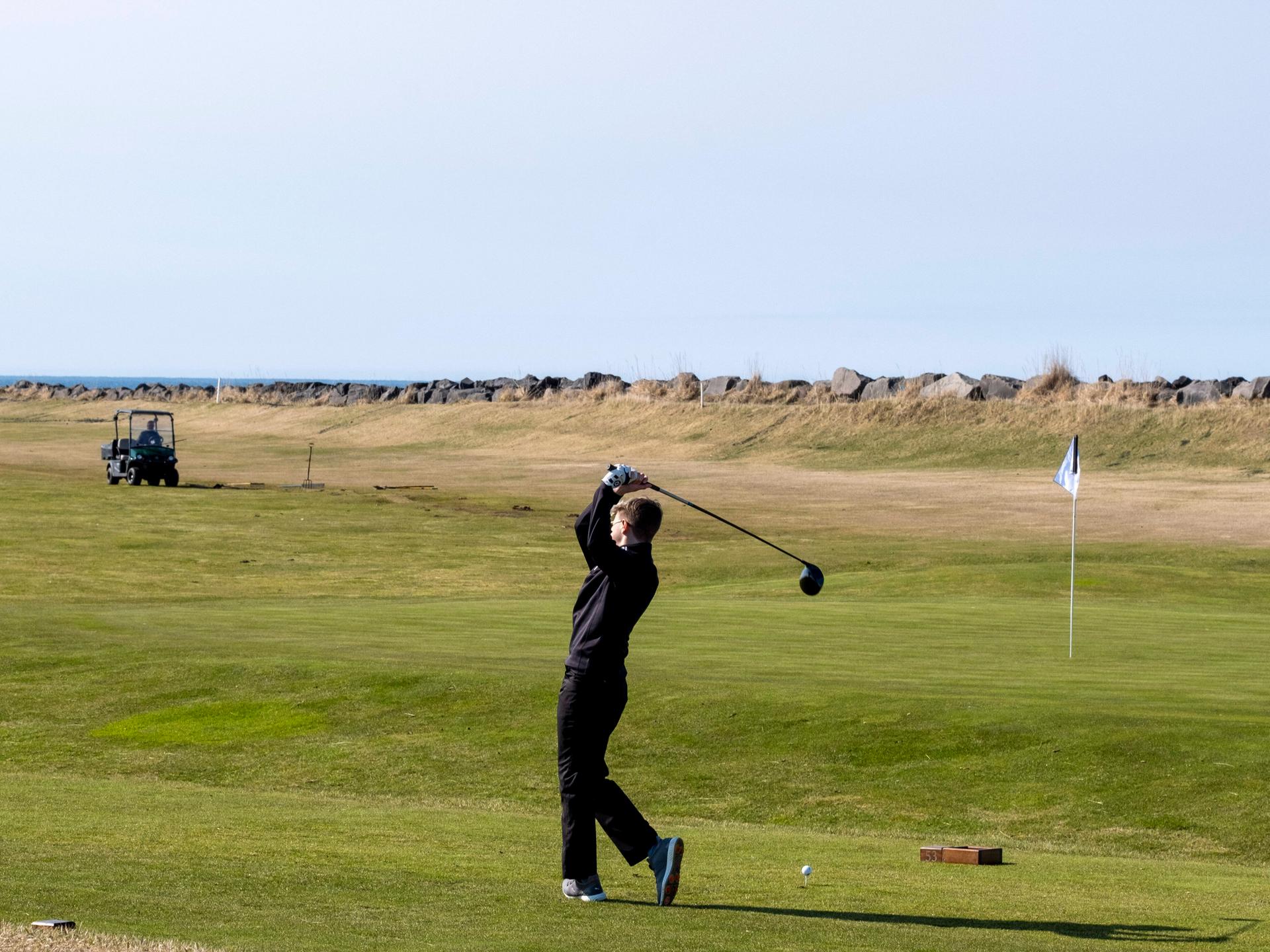 Ein Mann steht auf der Wiese und schwingt seinen Golfschläger durch die Luft.