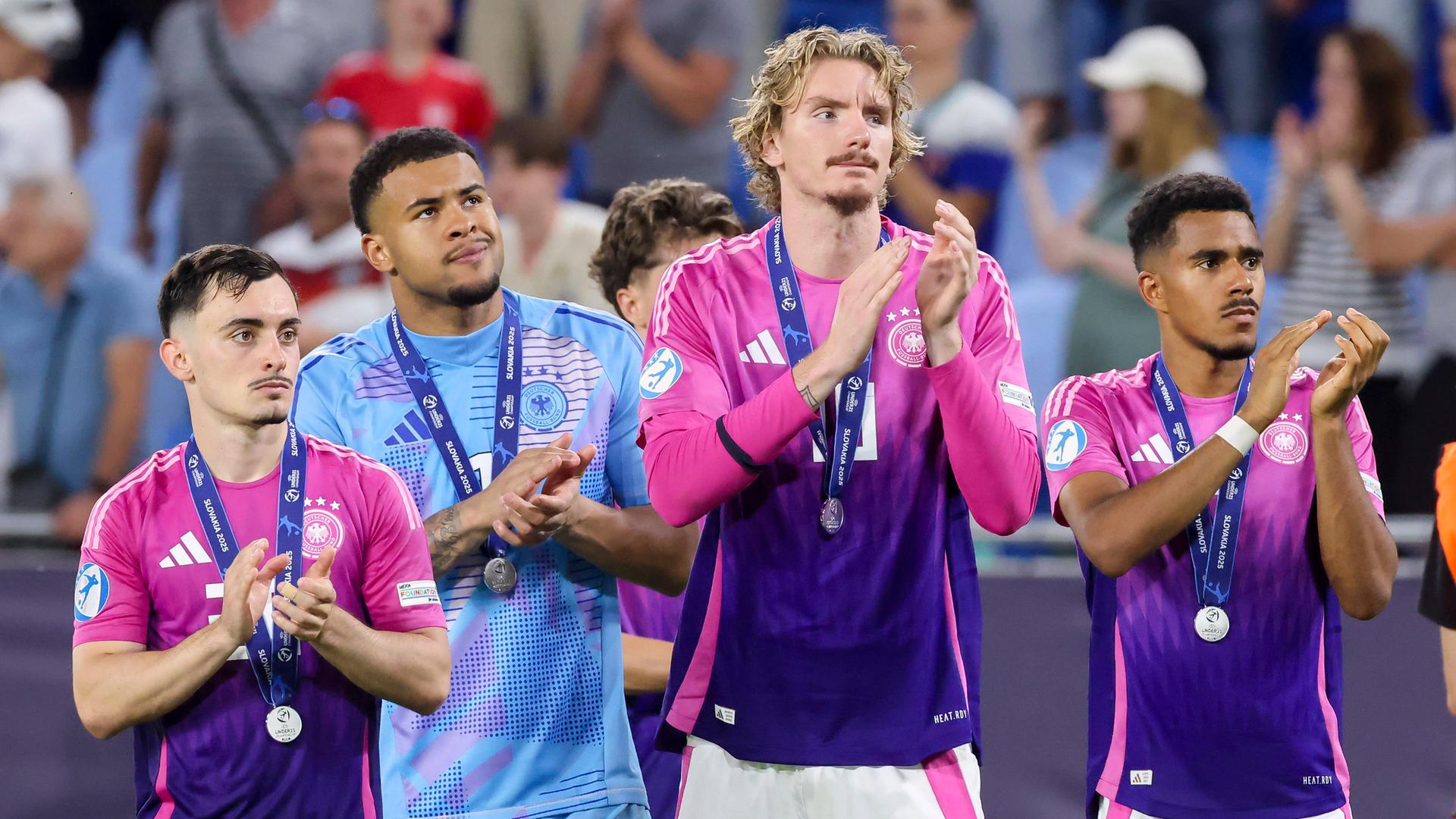 Die deutschen Fußballer Paul Nebel, Noah Atubolu, Nick Woltemade und Ansgar Knauff. Sie sind in einem Stadion und applaudieren dem Publikum. Um ihren Hals hängt eine Silber-Medaille. Sie sehen enttäuscht aus. Die deutschen Fußballer Paul Nebel, Noah Atubolu, Nick Woltemade und Ansgar Knauff. Sie sind in einem Stadion und applaudieren dem Publikum. Um ihren Hals hängt eine Silber-Medaille. Sie sehen enttäuscht aus.