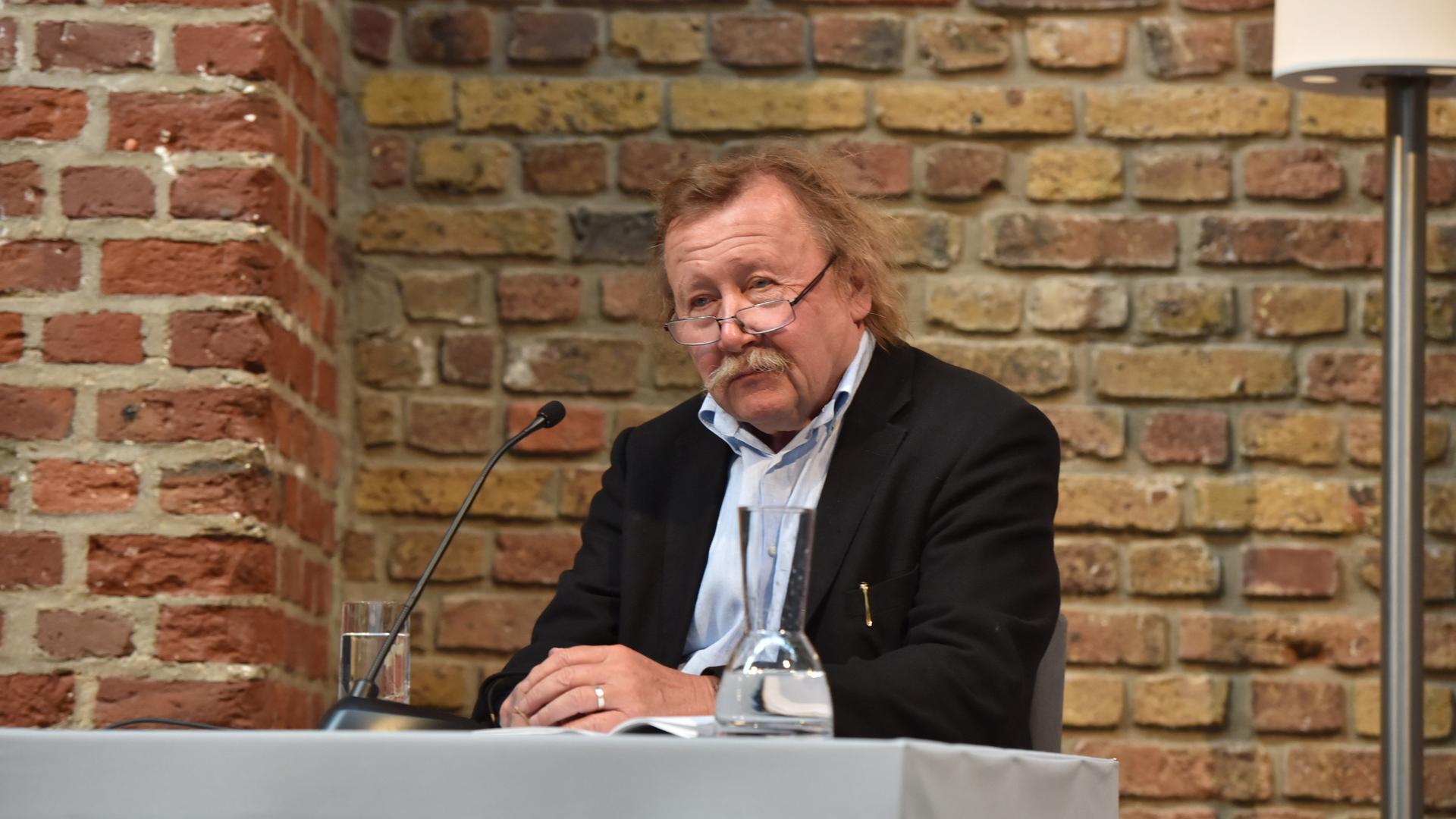 Der Autor und Philosoph Peter Sloterdijk an einem Tisch vor einer Backsteinwand sitzend