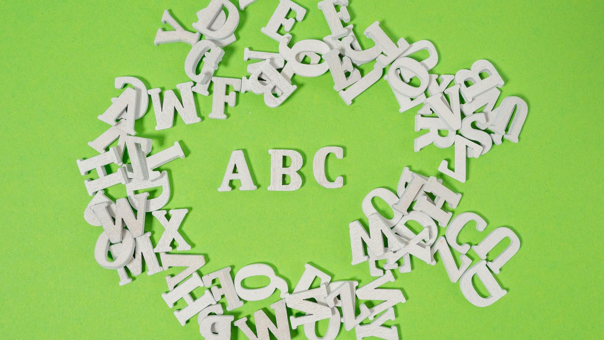 Weiße Holzbuchstaben wild auf grünem Untergrund verteilt - einzig die Buchstaben ABC kann man lesen.