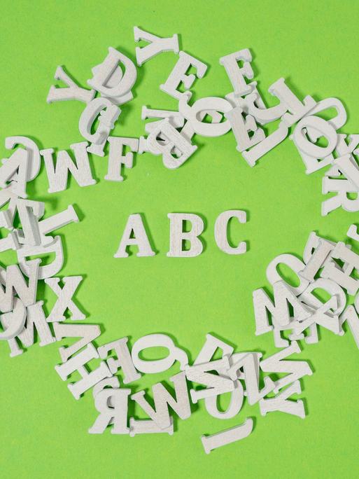 Weiße Holzbuchstaben wild auf grünem Untergrund verteilt - einzig die Buchstaben ABC kann man lesen.