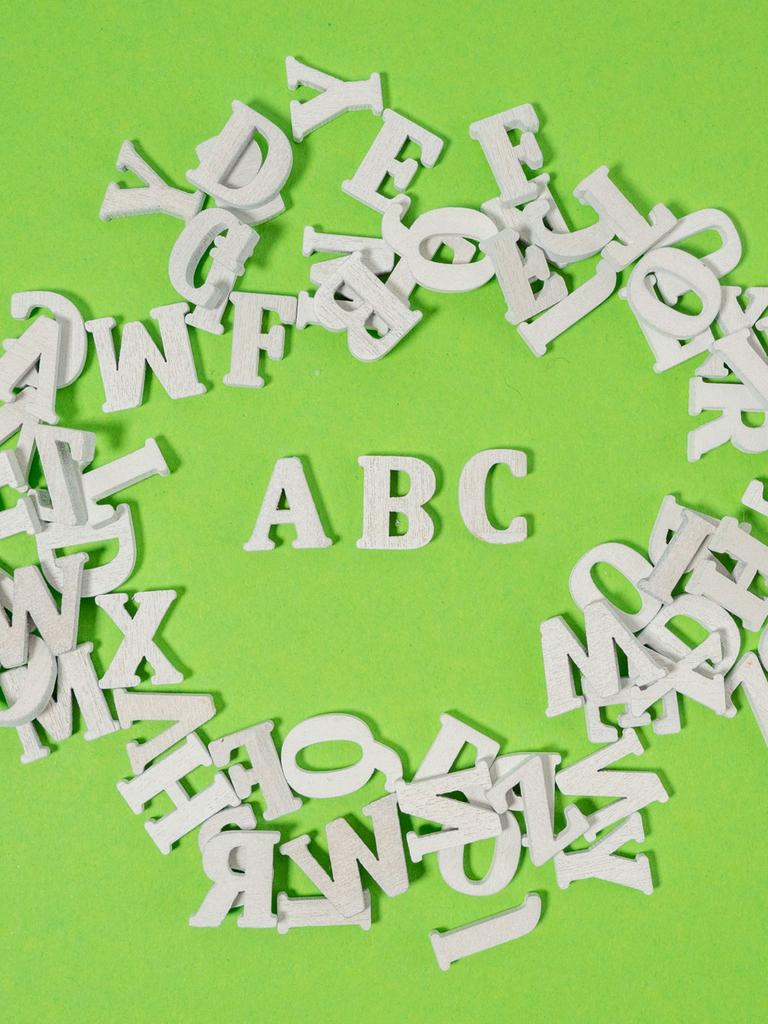 Weiße Holzbuchstaben wild auf grünem Untergrund verteilt - einzig die Buchstaben ABC kann man lesen.