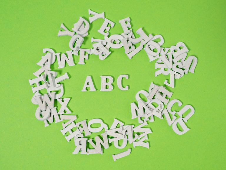 Weiße Holzbuchstaben wild auf grünem Untergrund verteilt - einzig die Buchstaben ABC kann man lesen.