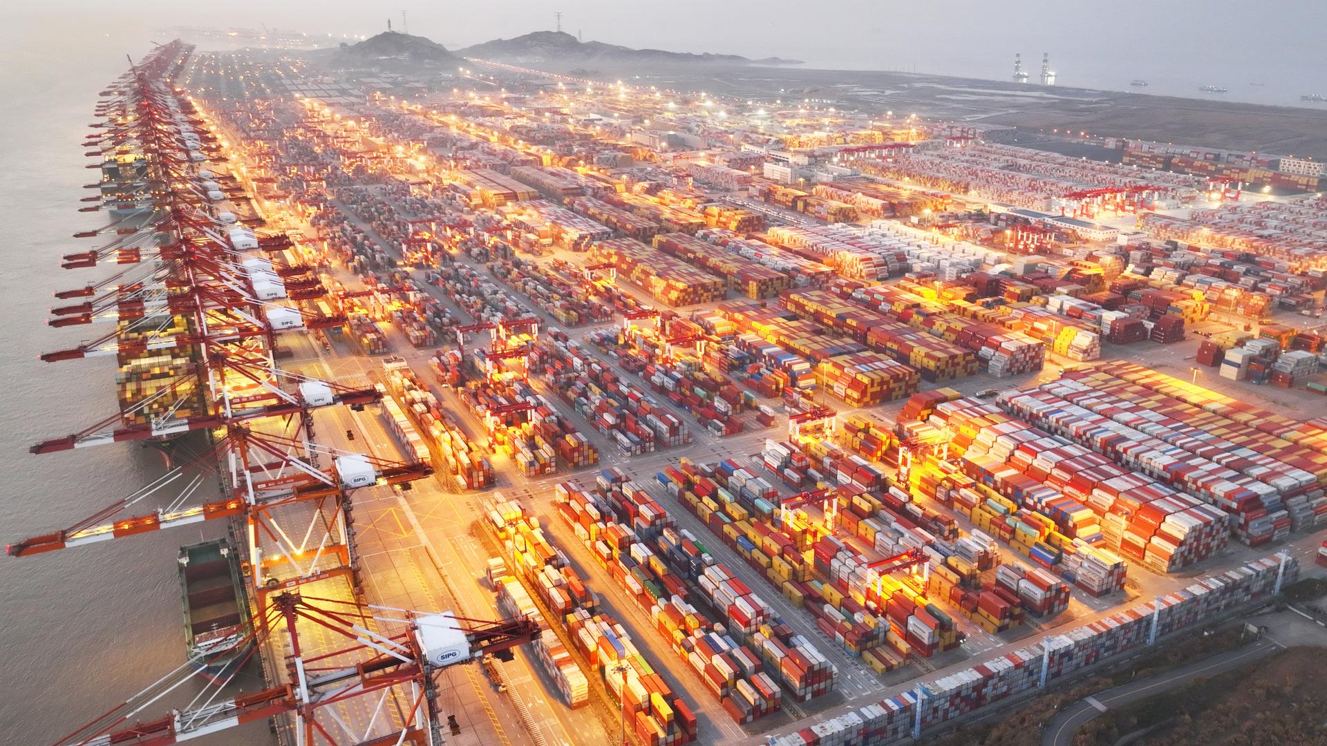 Blick aus großer Höhe auf den beleuchteten Containerhafen im Morgengrauen.