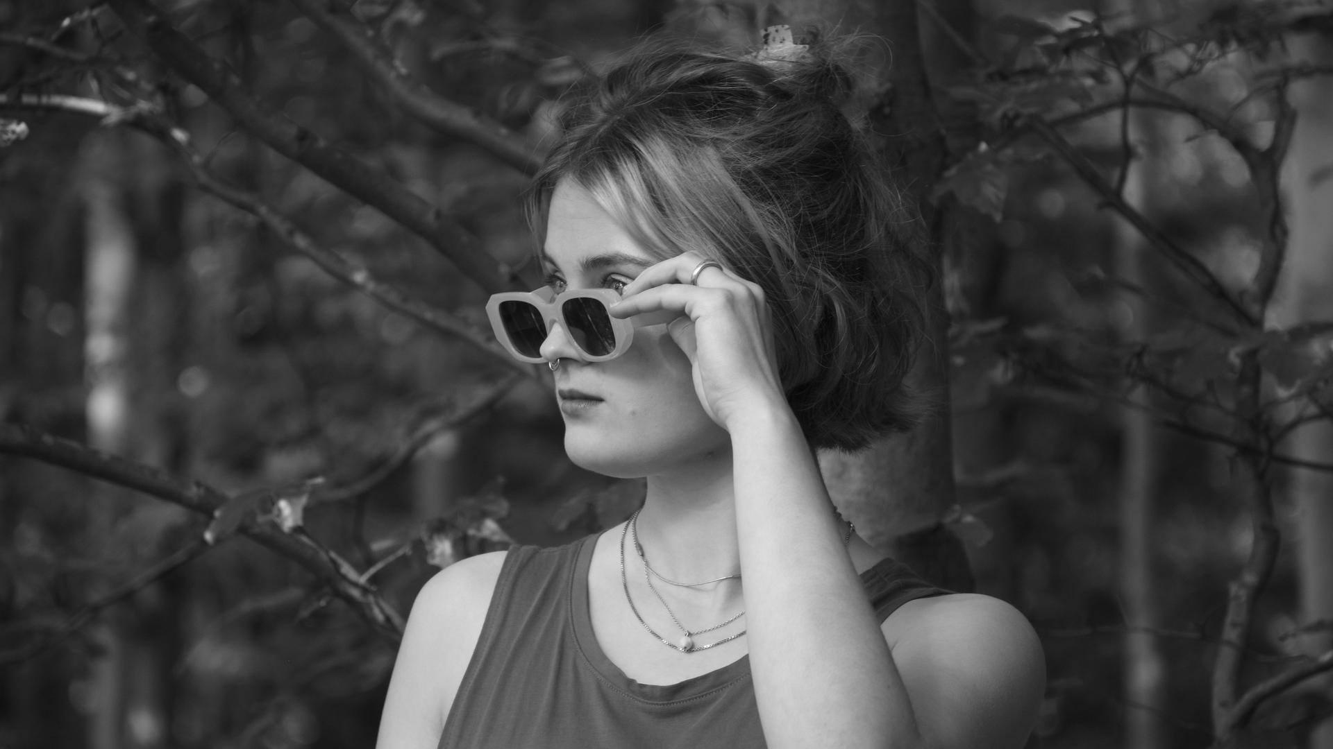 Eine junge Frau hält ihre Sonnenbrille, während sie über den Rand in die Ferne schaut Eine junge Frau hält ihre Sonnenbrille, während sie über den Rand in die Ferne schaut