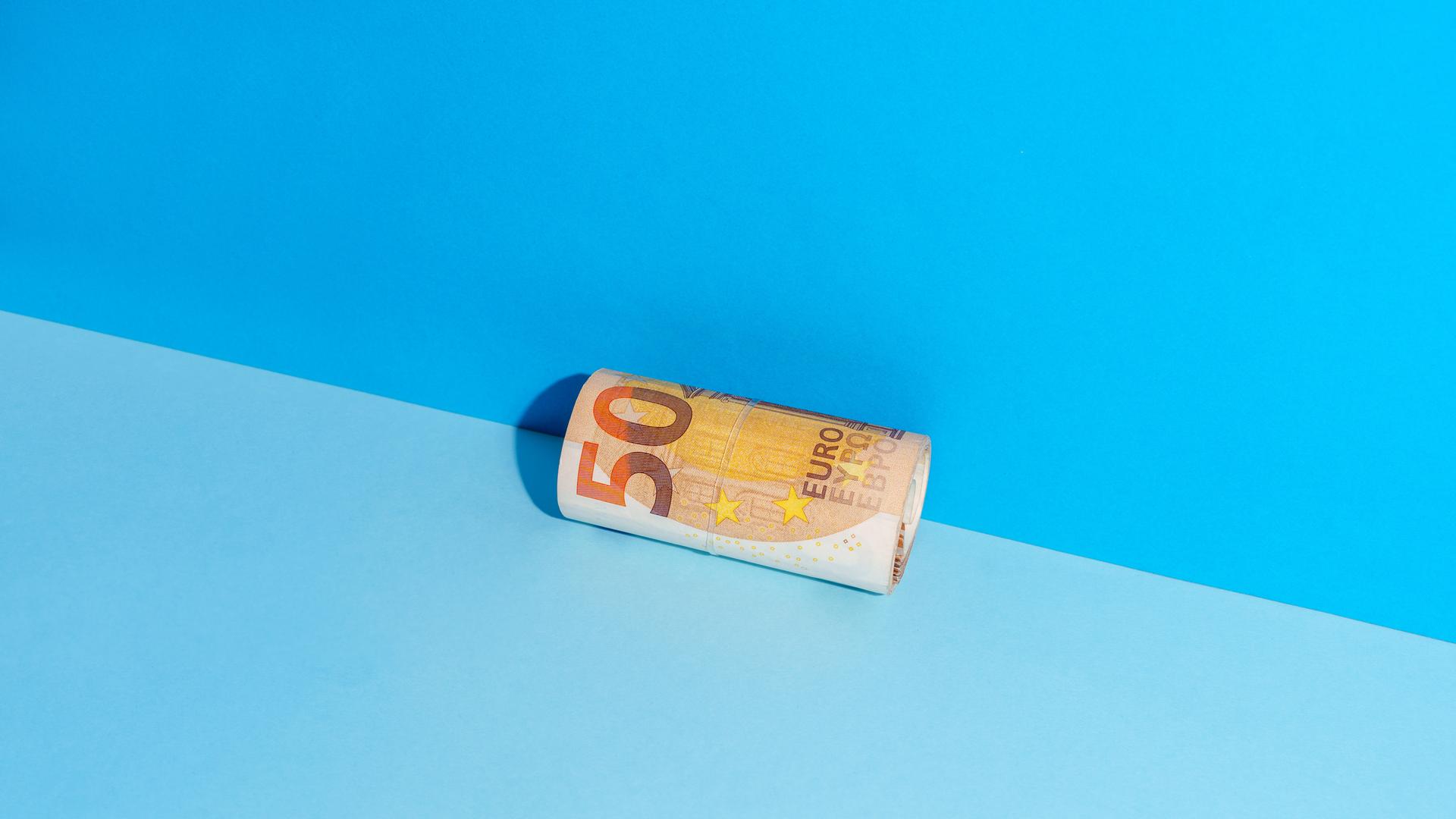 Ein zusammengerollter Fünfzigeuroschein liegt in der Ecke zwischen einer blauen Wand und einem blauen Boden.