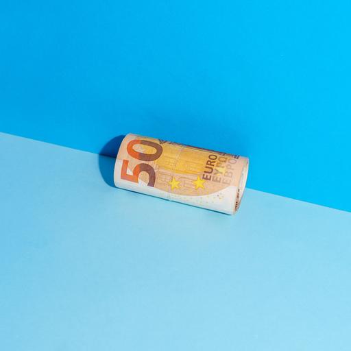 Ein zusammengerollter Fünfzigeuroschein liegt in der Ecke zwischen einer blauen Wand und einem blauen Boden.