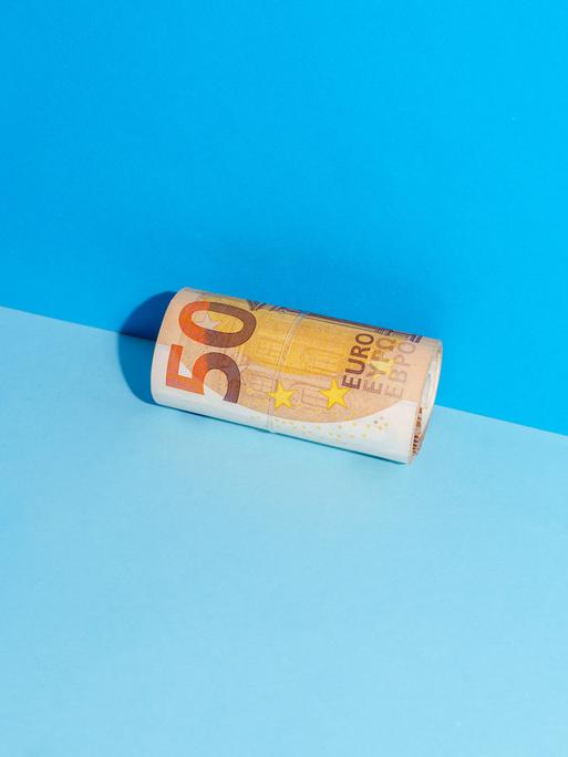 Ein zusammengerollter Fünfzigeuroschein liegt in der Ecke zwischen einer blauen Wand und einem blauen Boden.