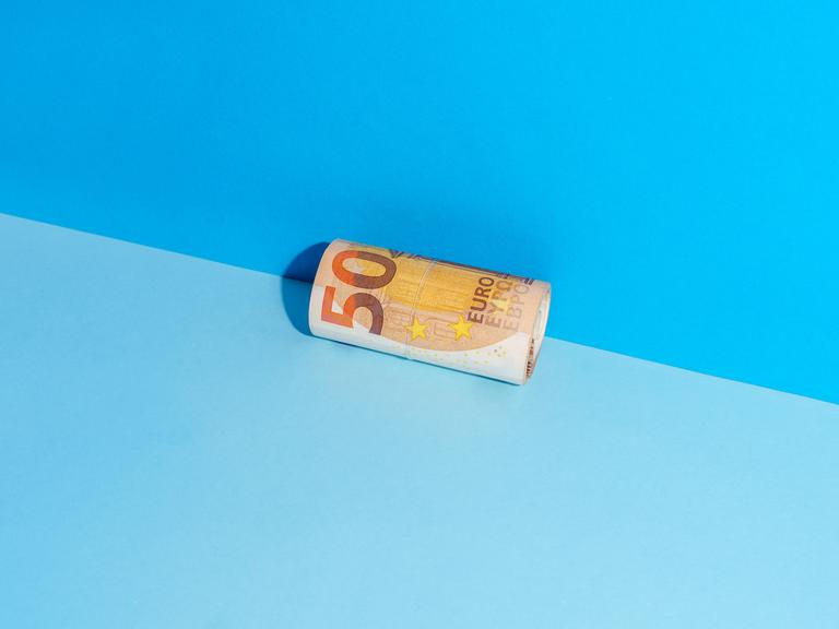 Ein zusammengerollter Fünfzigeuroschein liegt in der Ecke zwischen einer blauen Wand und einem blauen Boden.