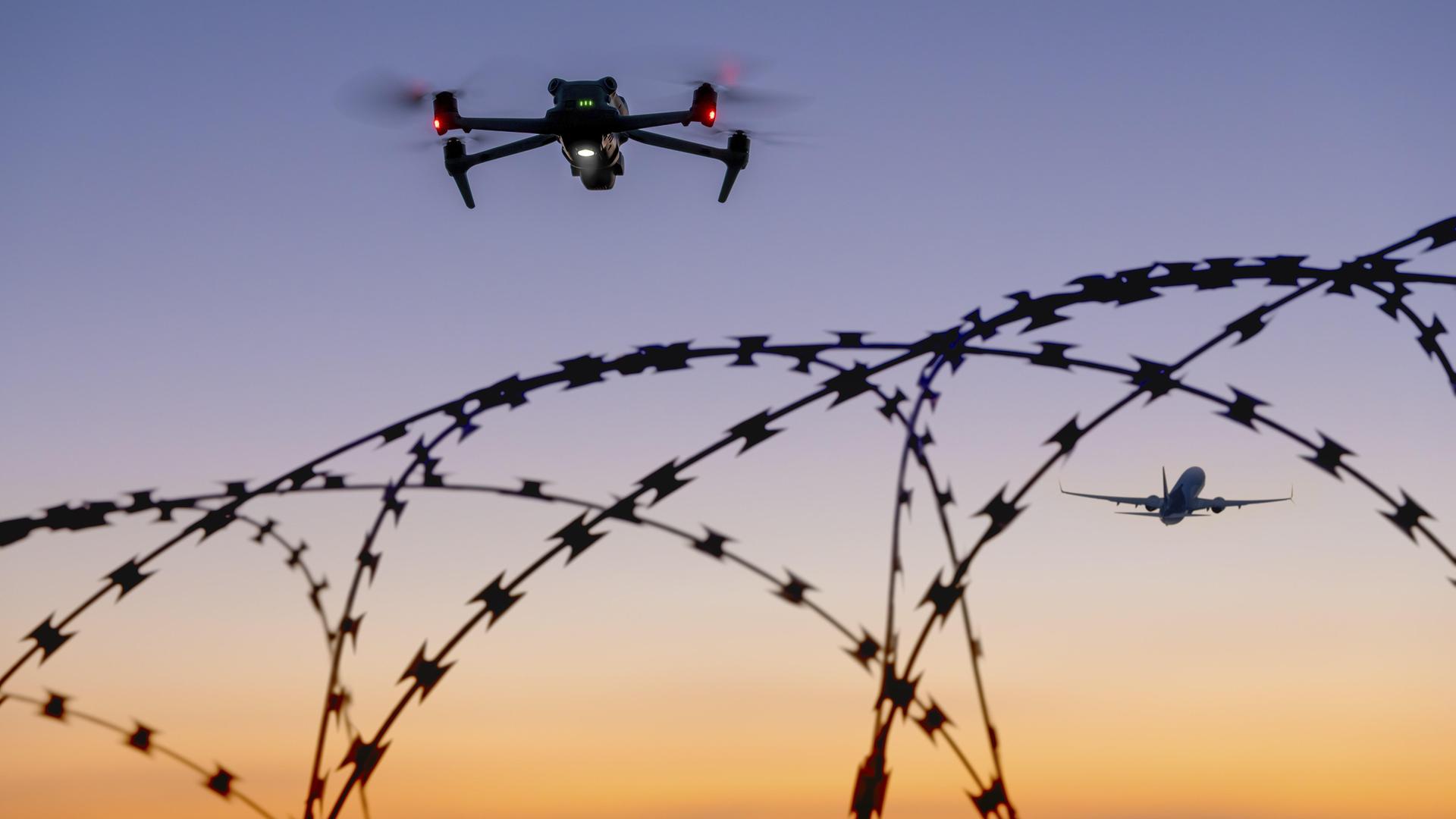 Eine Drohne und ein Flugzeug am Himmel über Stacheldraht bei Sonnenuntergang Eine Drohne und ein Flugzeug am Himmel über Stacheldraht bei Sonnenuntergang