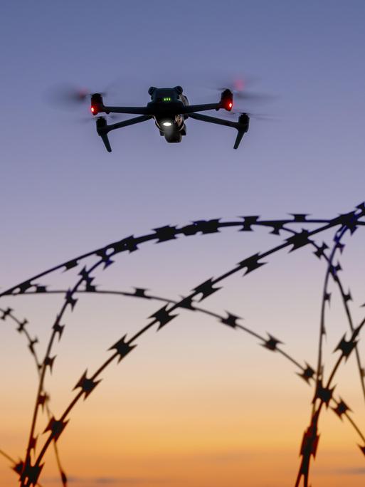 Eine Drohne und ein Flugzeug am Himmel über Stacheldraht bei Sonnenuntergang
