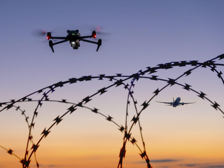 Eine Drohne und ein Flugzeug am Himmel über Stacheldraht bei Sonnenuntergang