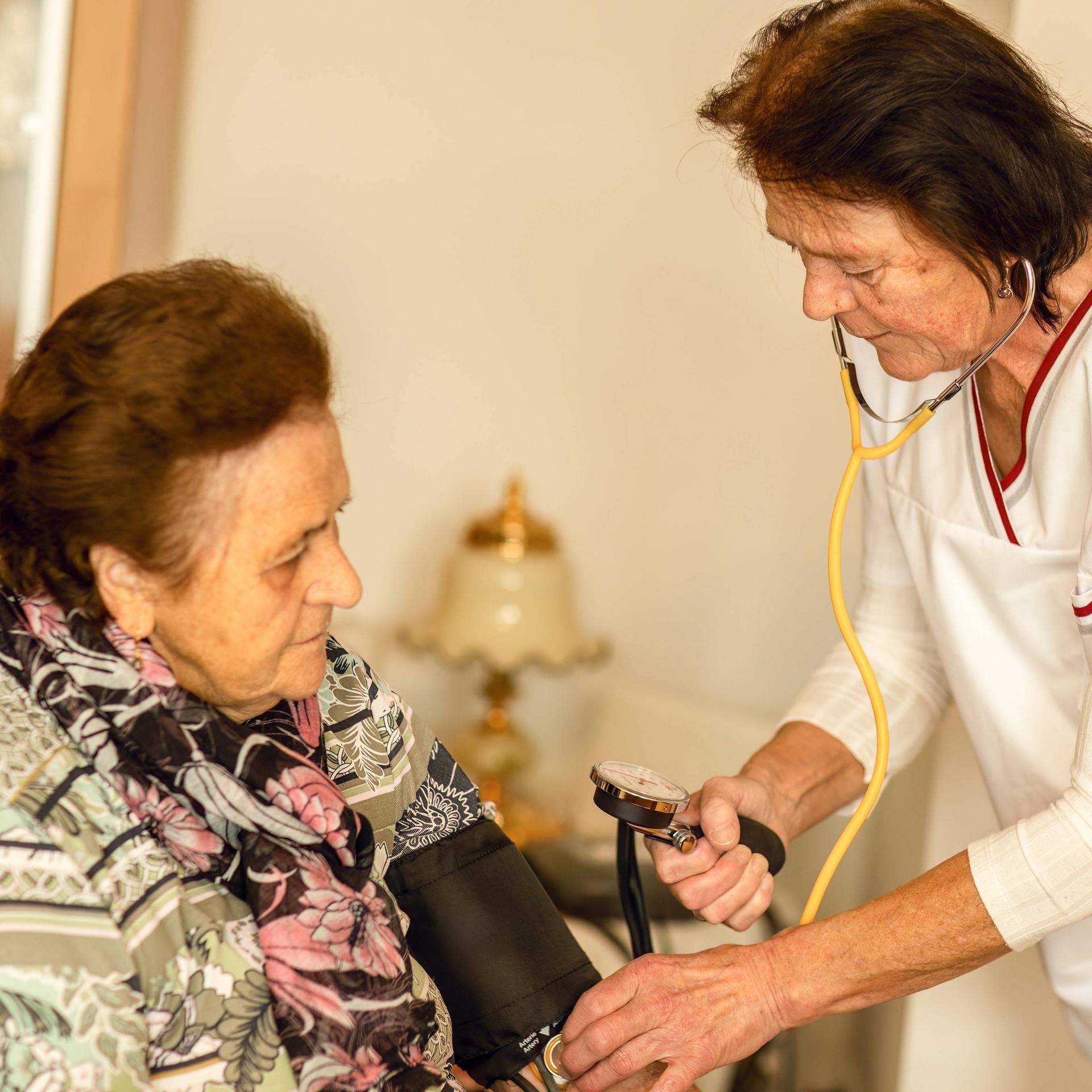 Eine häusliche Krankenschwester misst den Blutdruck einer älteren Frau im Rahmen der Herz-Kreislauf-Überwachung. 
