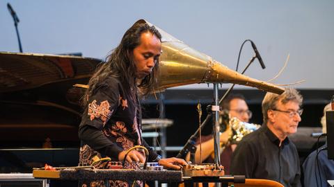 Ein indonesischer Musiker mit langen dunklen Haaren steht am Regler eines selbstgebauten Instruments